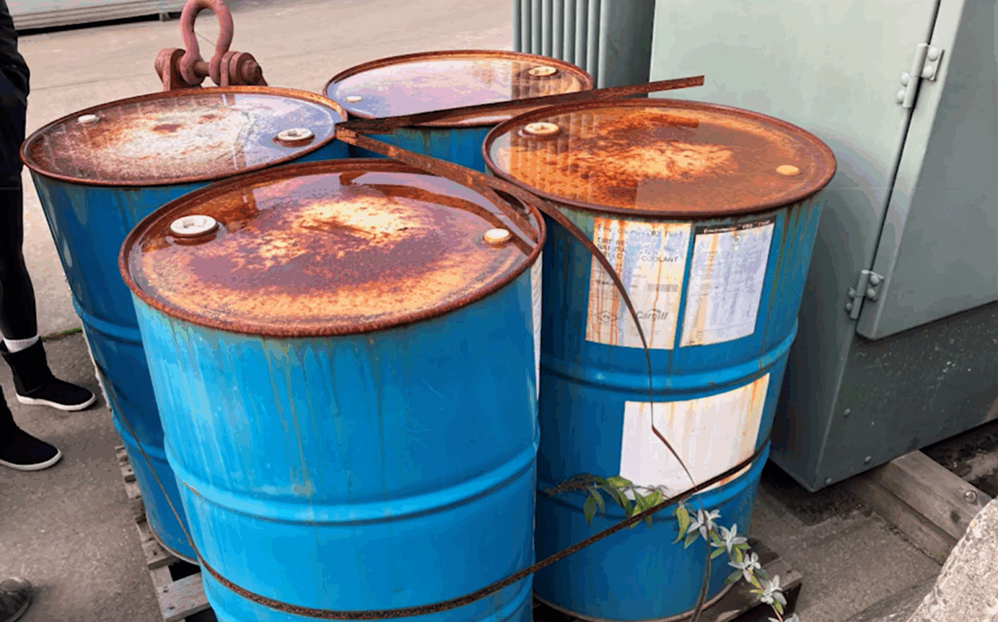 4 rusty blue metal 55 gallon drums stored outdoors on a pallet without secondary containment